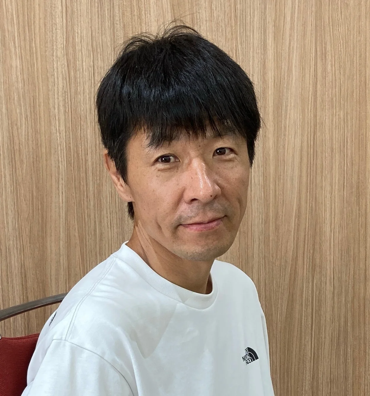 白いTシャツを着たアジア人男性がカメラ目線で座っているポートレート。